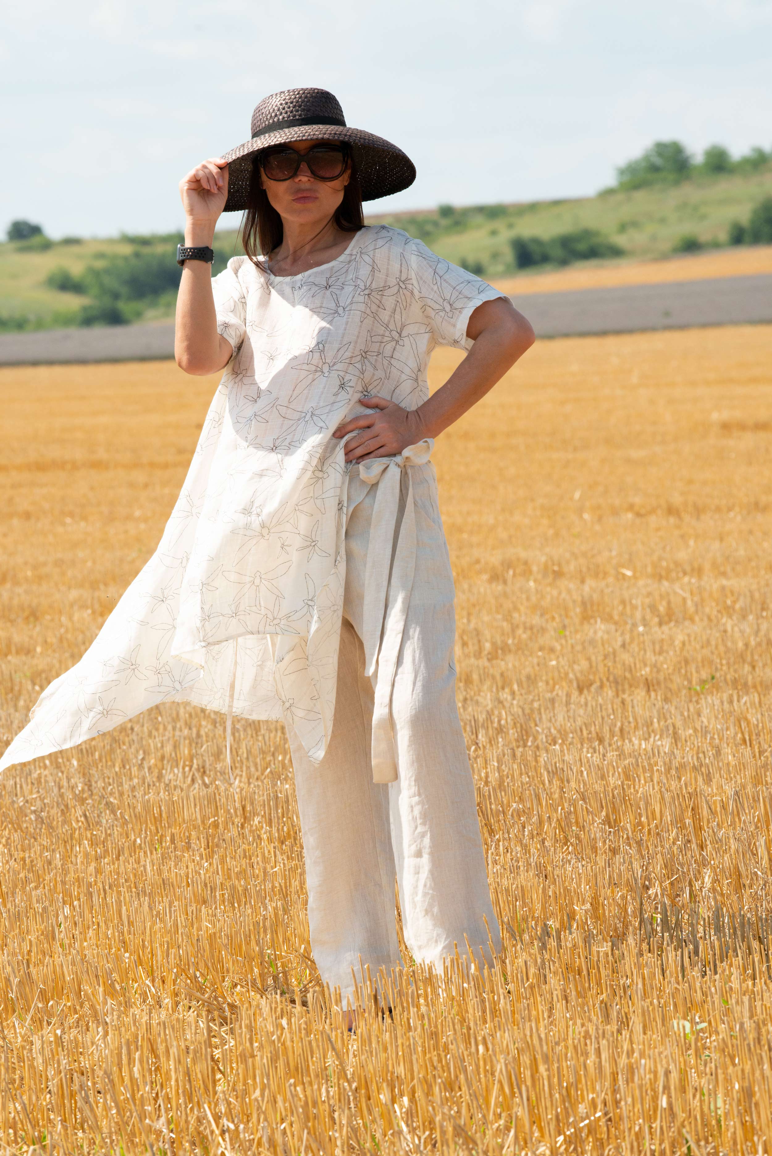 Woman in a white dress and black hat standing in a field of golden wheat.