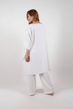Woman wearing a white long-sleeve top and wide-leg pants on a white background
