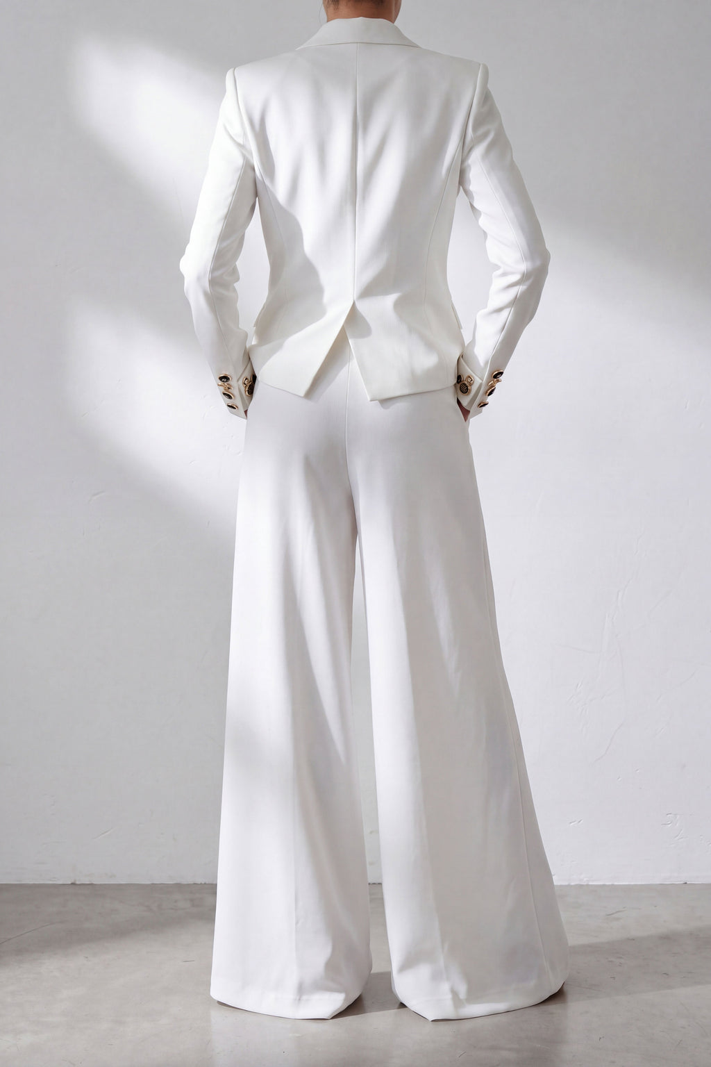 Person wearing a white suit standing against a plain background