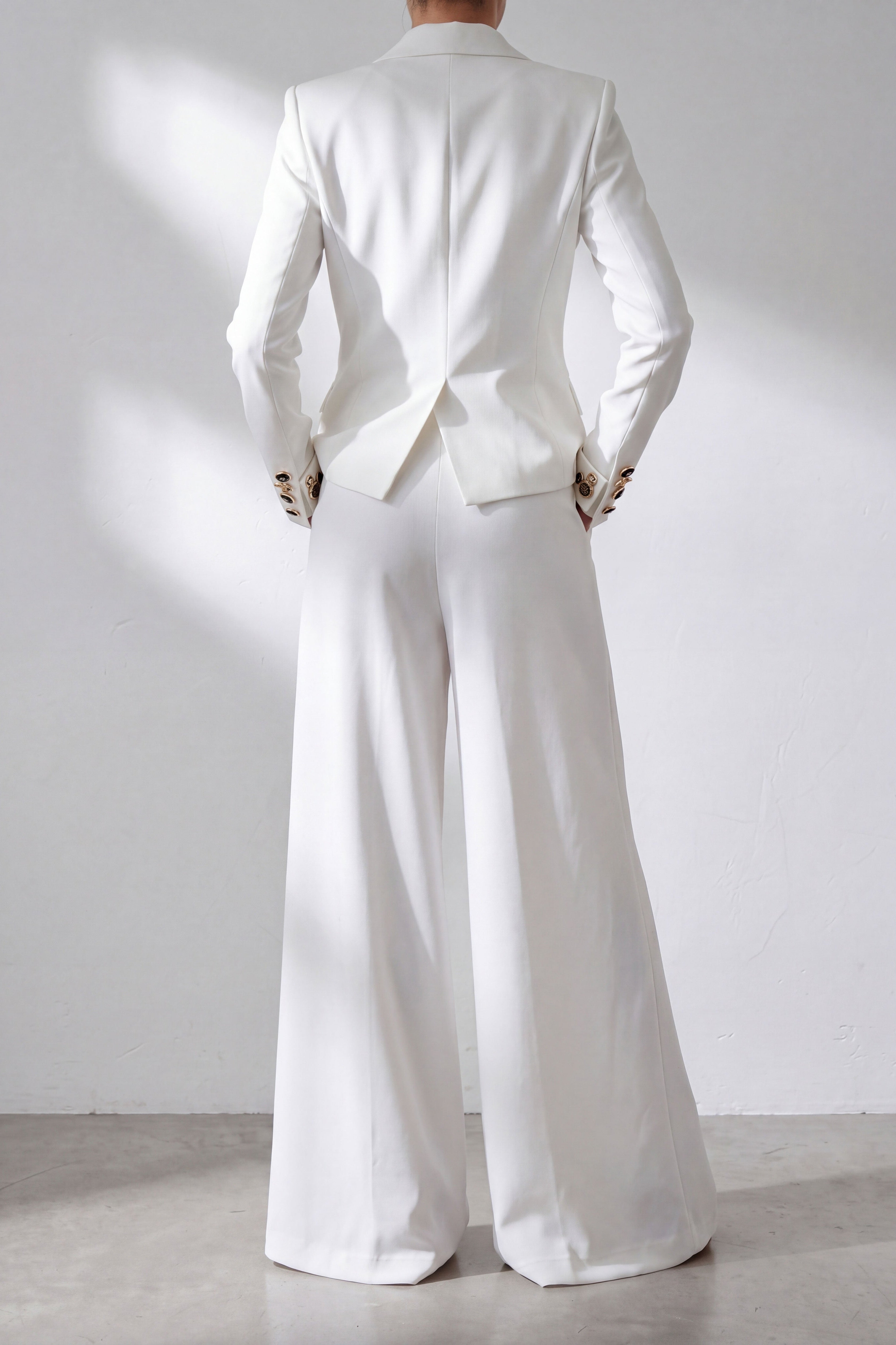 Person wearing a white suit standing against a plain background