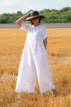 Person wearing a white jumpsuit and black hat standing in a field of golden wheat.