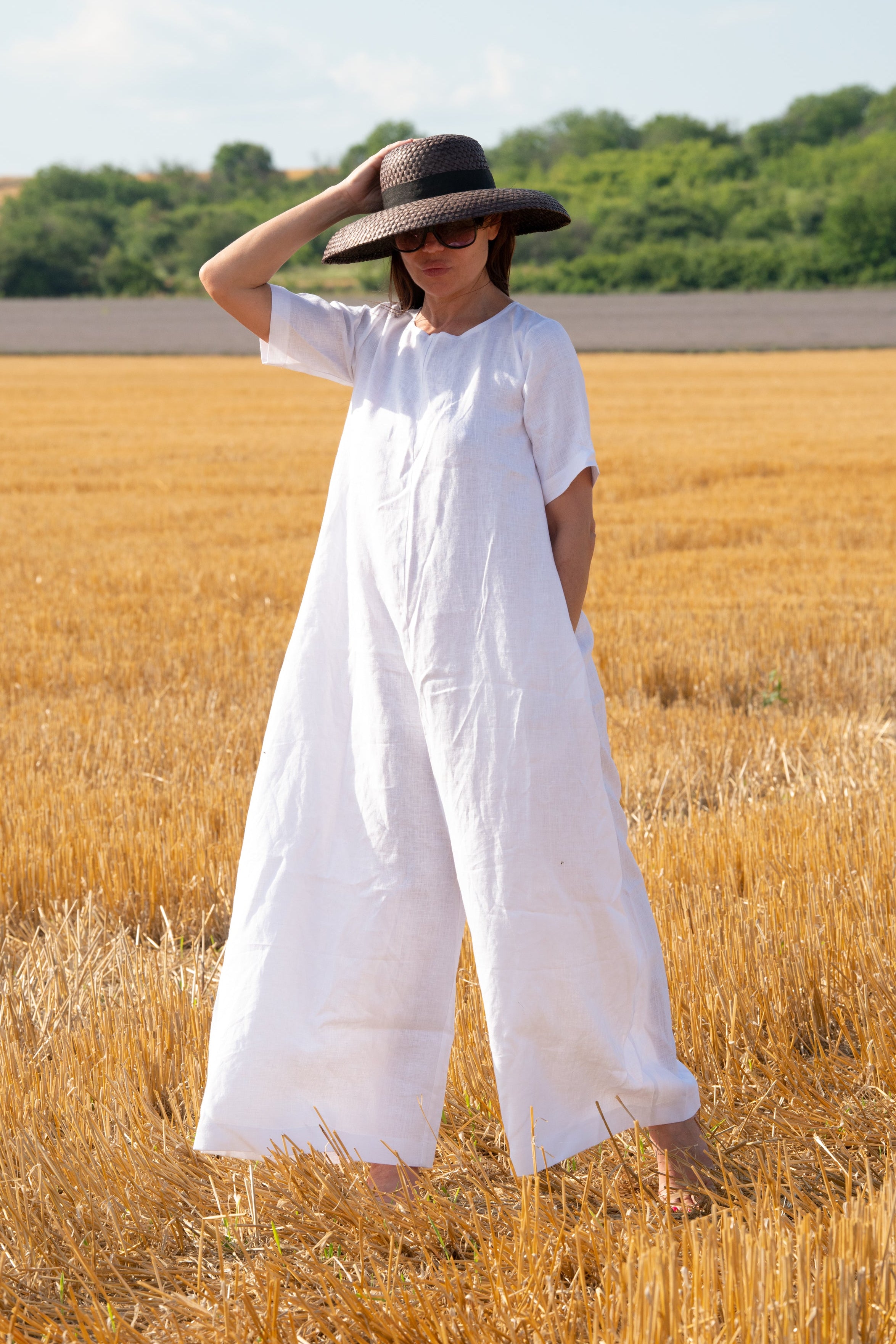Person wearing a white jumpsuit and black hat standing in a field of golden wheat.