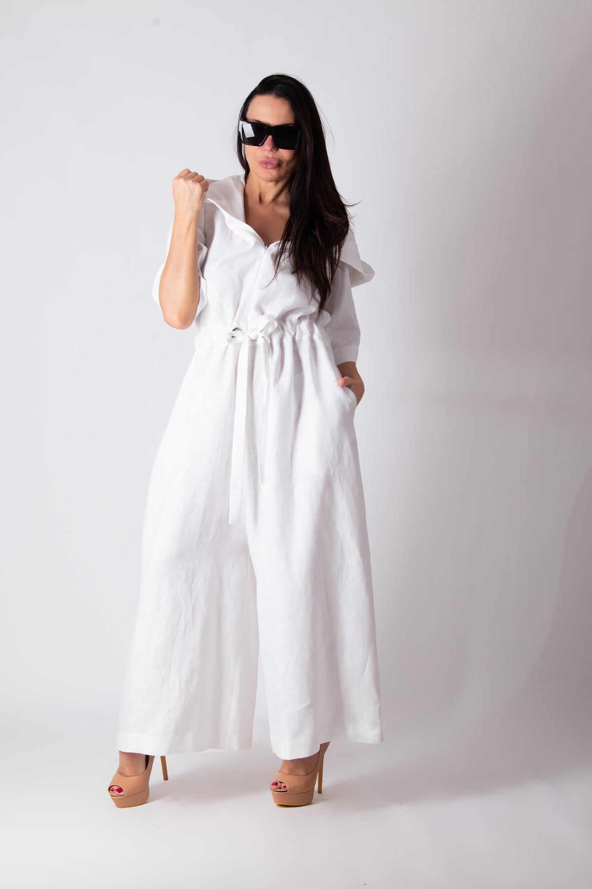 Woman wearing a white jumpsuit with ruffled sleeves against a plain background