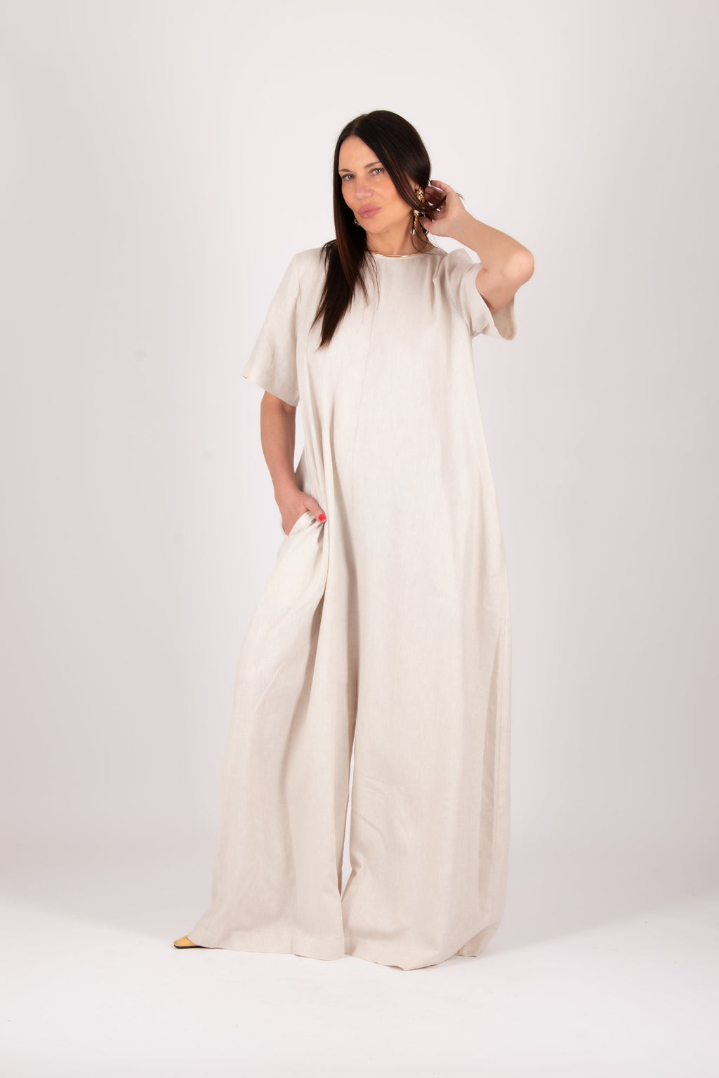Woman wearing a long, light-colored jumpsuit  against a white background