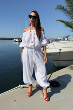 Woman in a white outfit standing by a waterfront with boats and palm trees.