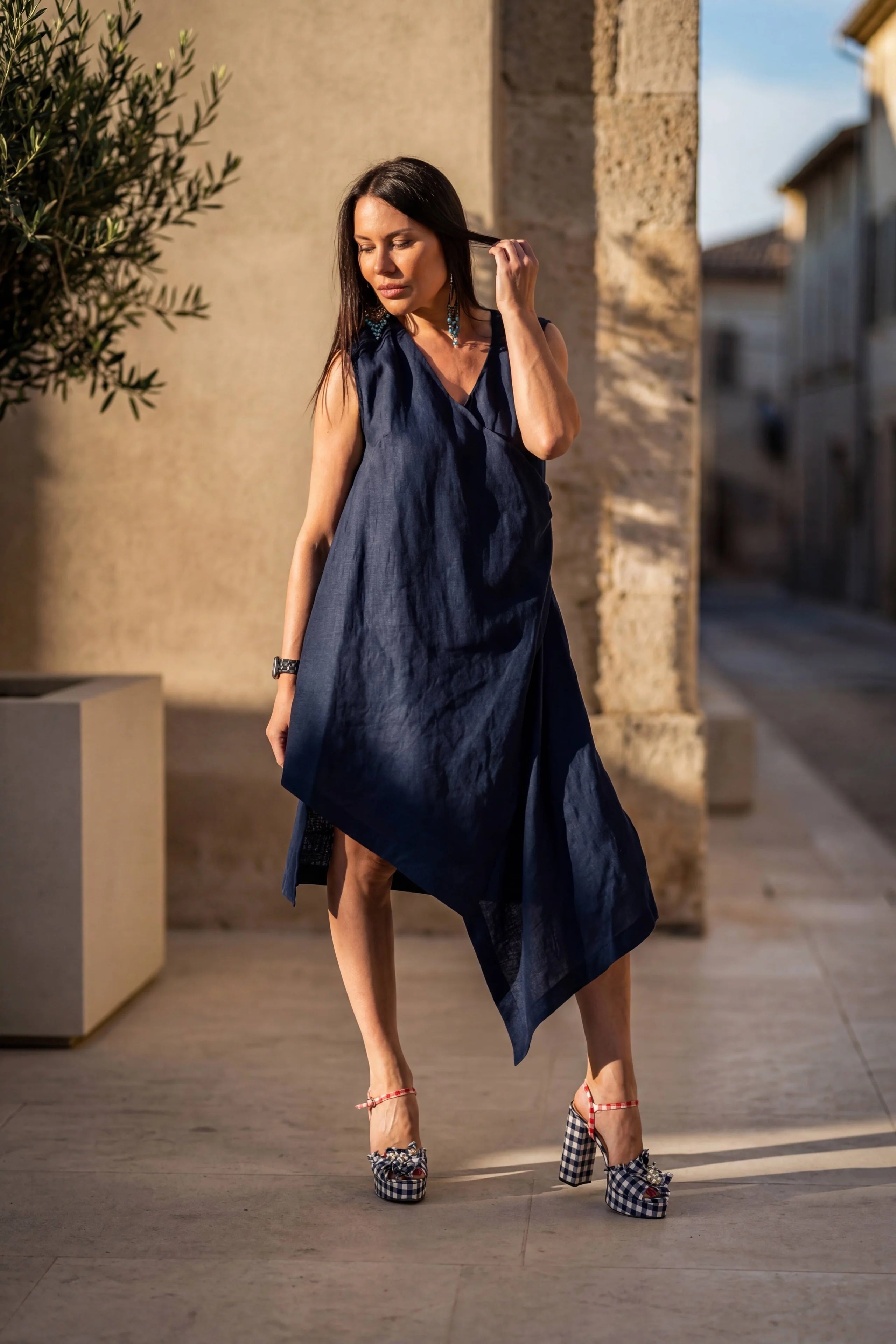 Woman in a navy blue dress standing on a street with buildings and plants in the background