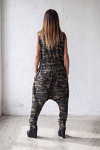 Person wearing a camouflage jumpsuit standing against a white wall.