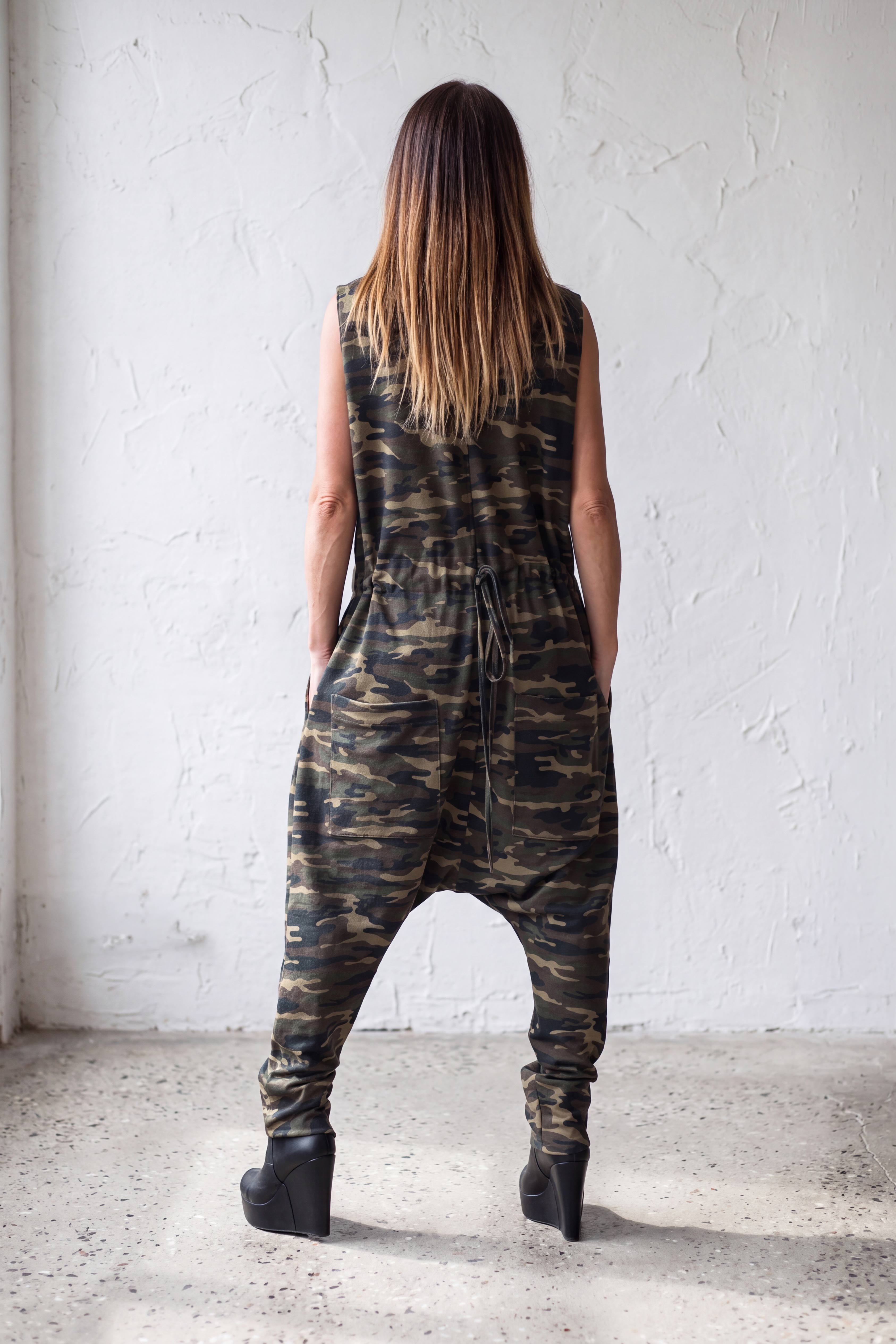 Person wearing a camouflage jumpsuit standing against a white wall.