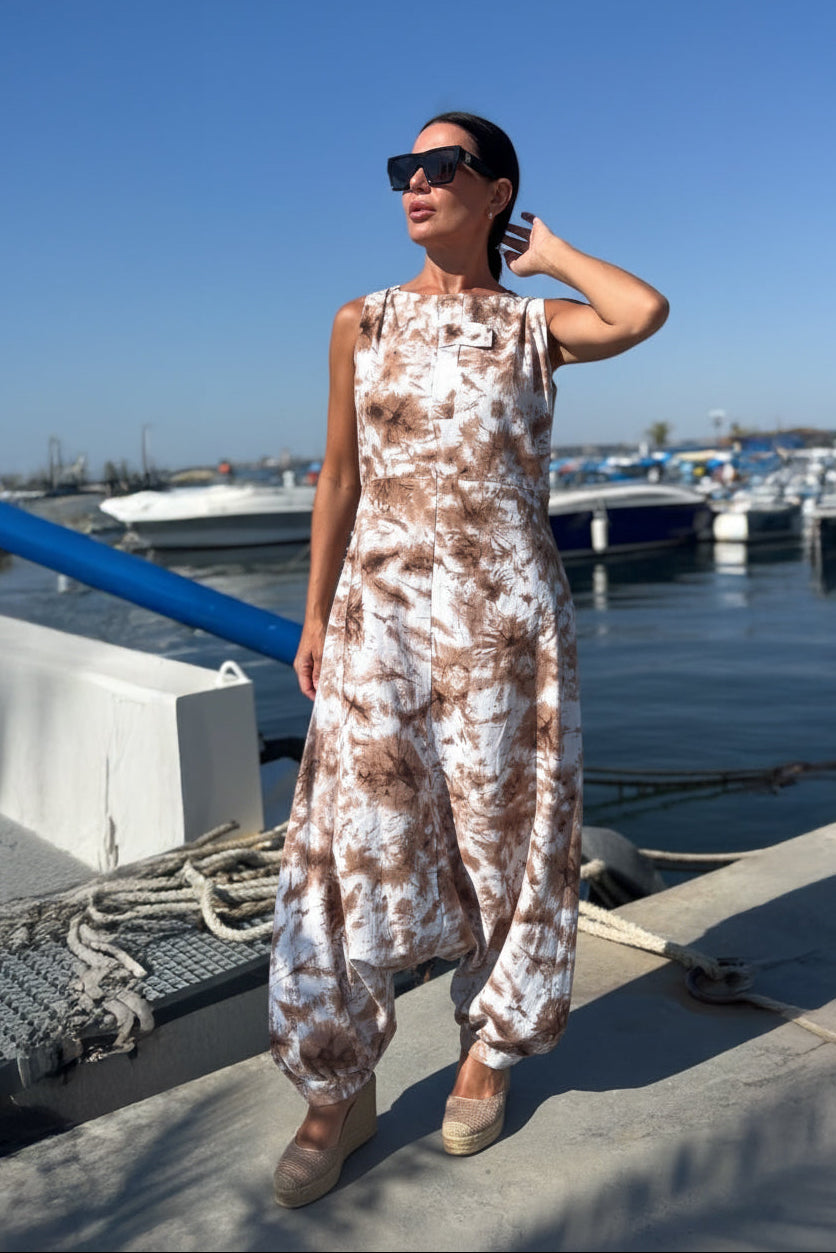 Woman in a patterned dress standing on a dock with boats in the background