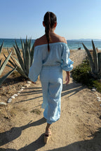 Woman in light blue outfit walking on a sandy path with ocean view