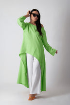 Woman wearing a bright green long-sleeve top and white pants on a plain background