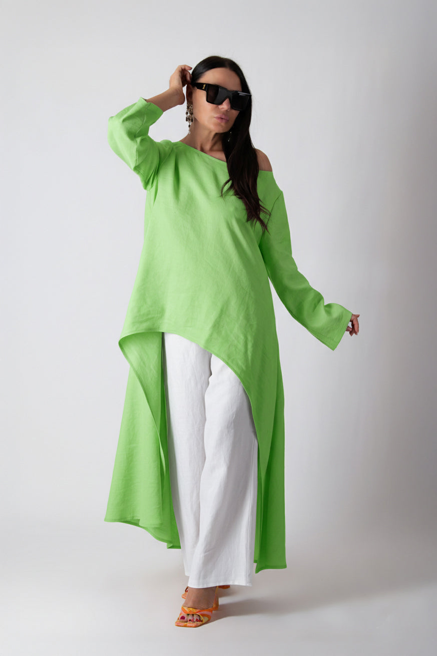 Woman wearing a bright green long-sleeve top and white pants on a plain background