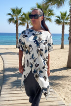 Woman walking on a wooden boardwalk by the beach with palm trees and ocean in the background.