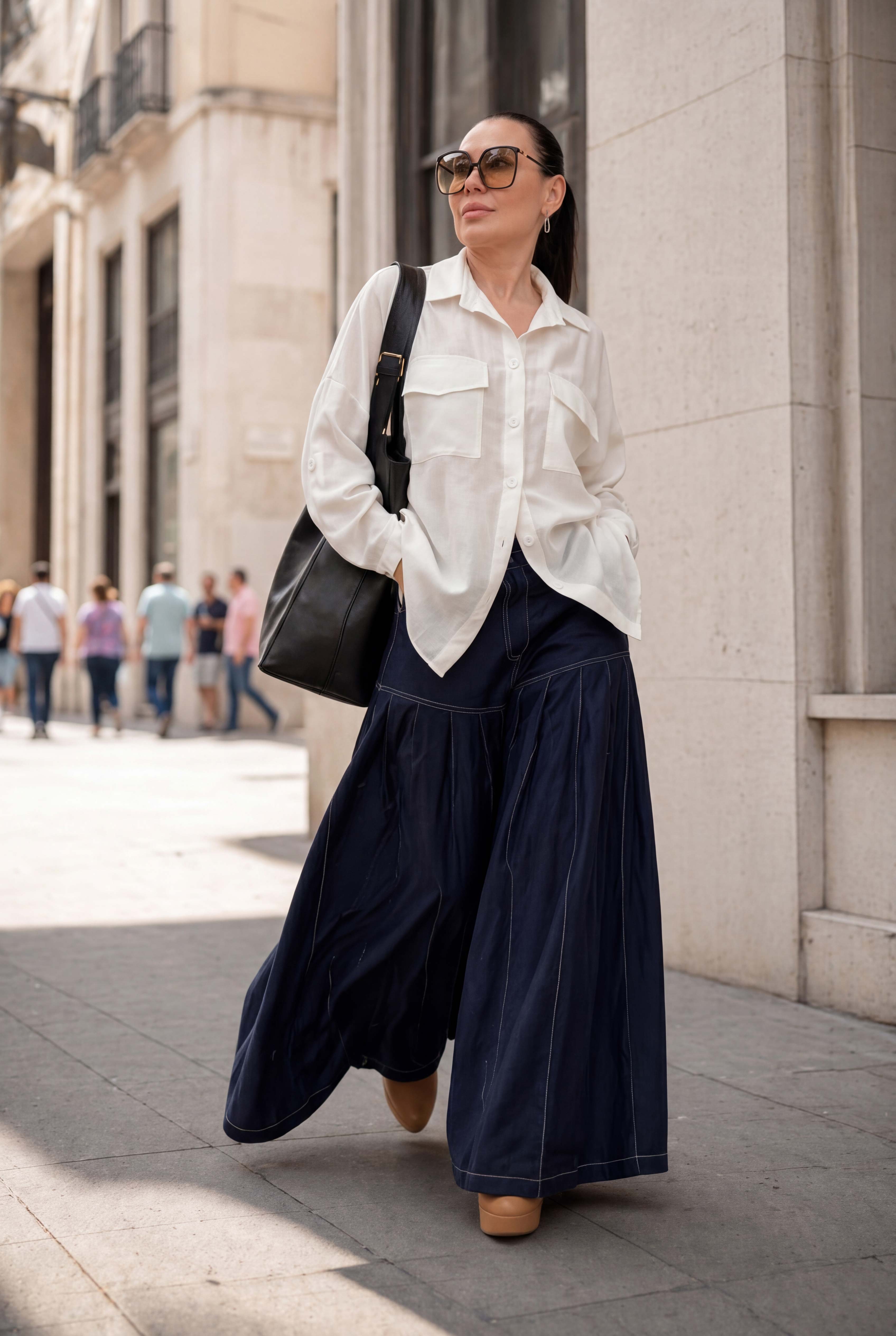 Woman in a white shirt and navy pants walking on a city street.