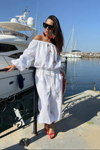 Woman in a white outfit standing by a dock with boats in the background