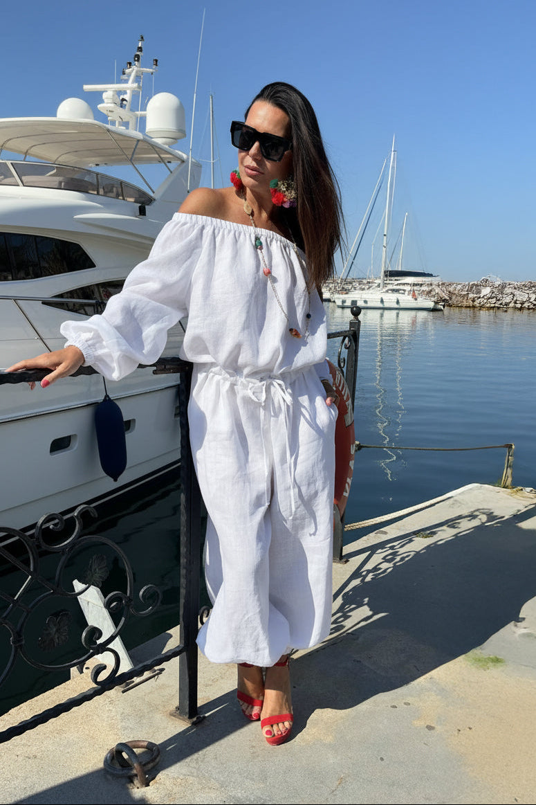 Woman in a white outfit standing by a dock with boats in the background
