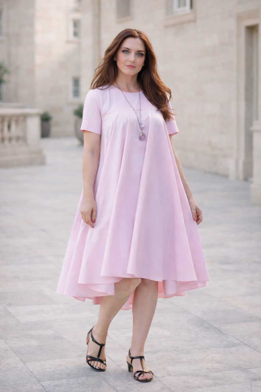 Woman wearing a pink dress standing on a stone pathway.