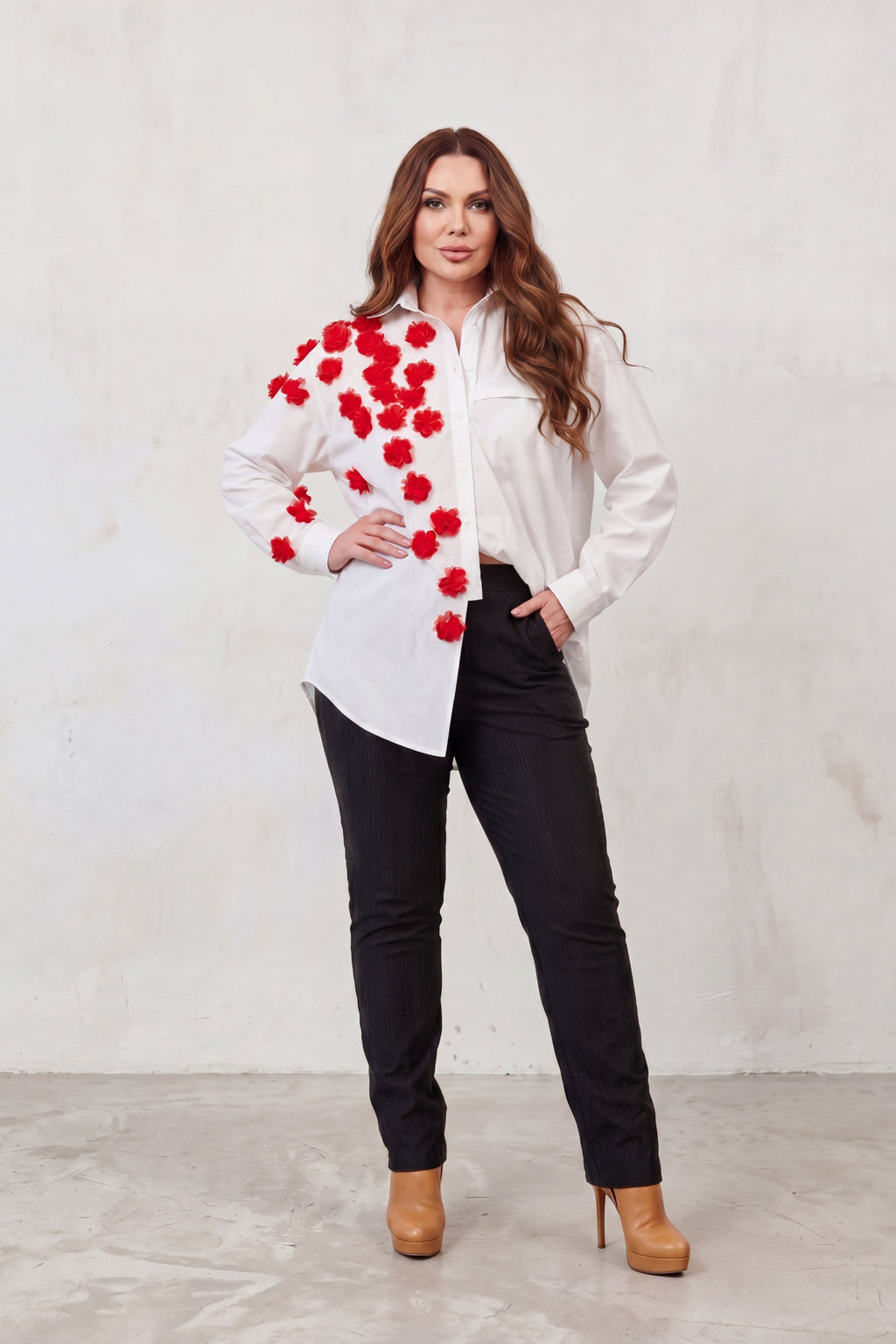 Woman wearing a white blouse with red floral patterns and black pants against a light gray background