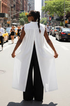 Person wearing a white sleeveless top and black pants on a city street.