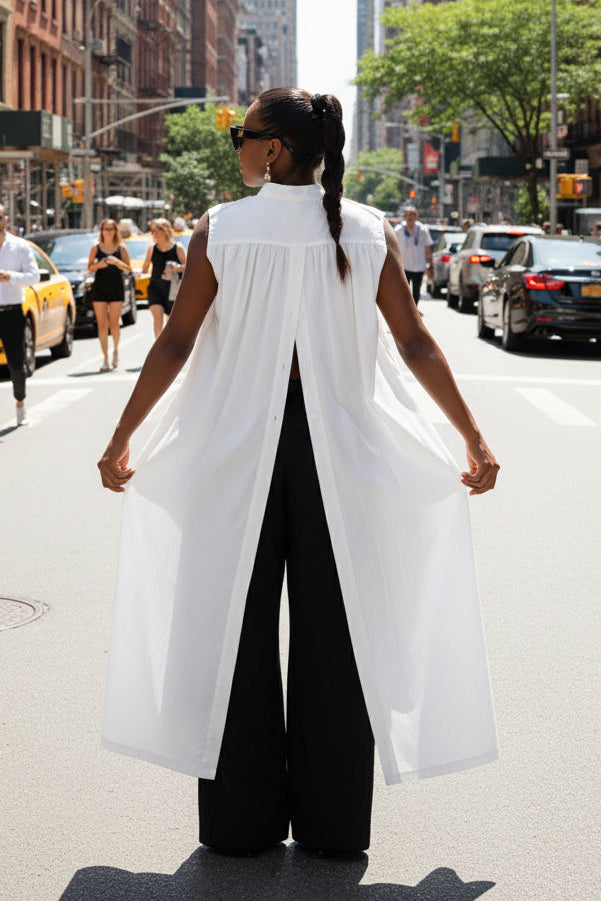 Person wearing a white sleeveless top and black pants on a city street.