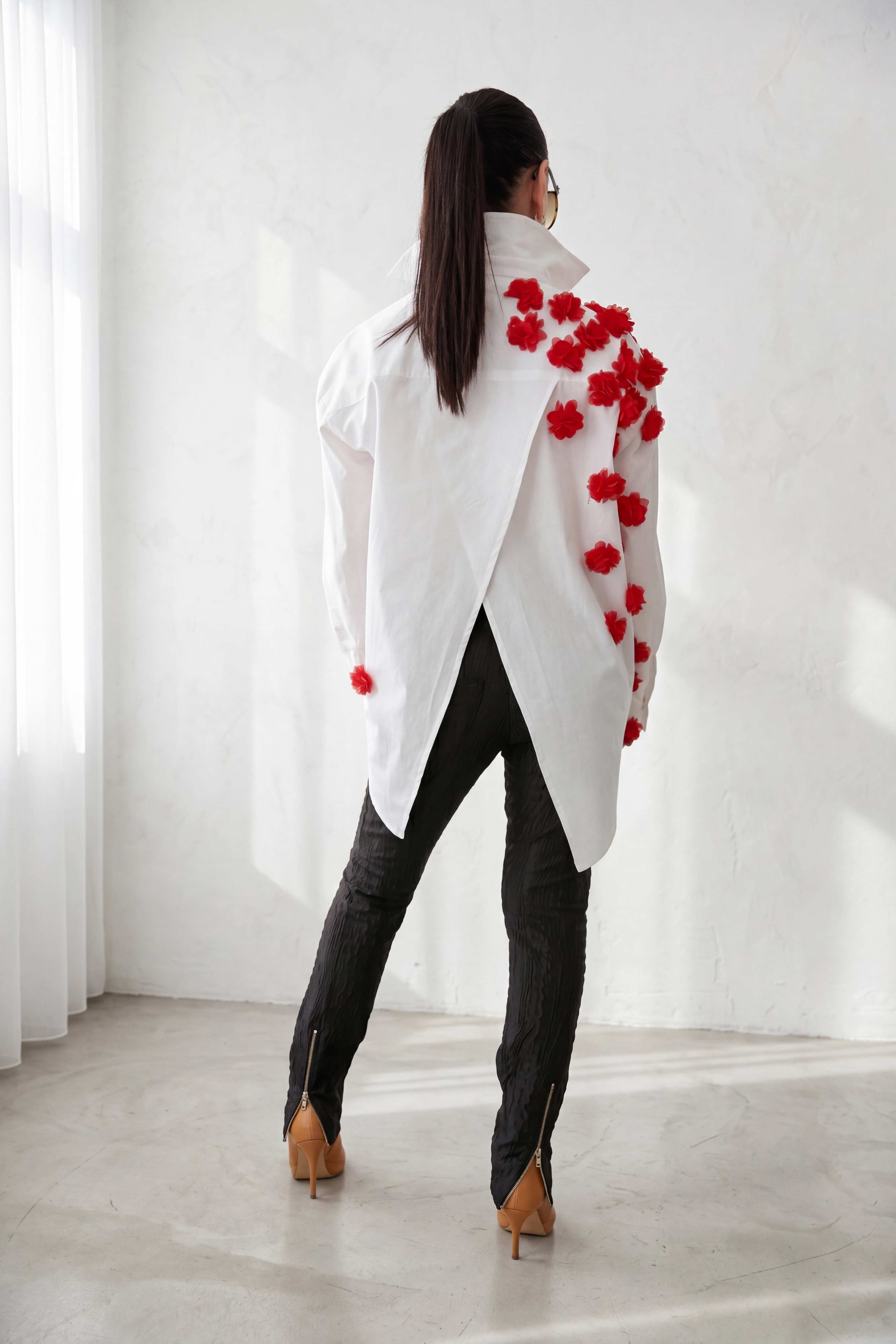 Woman wearing a white coat with red floral patterns, standing against a white background.