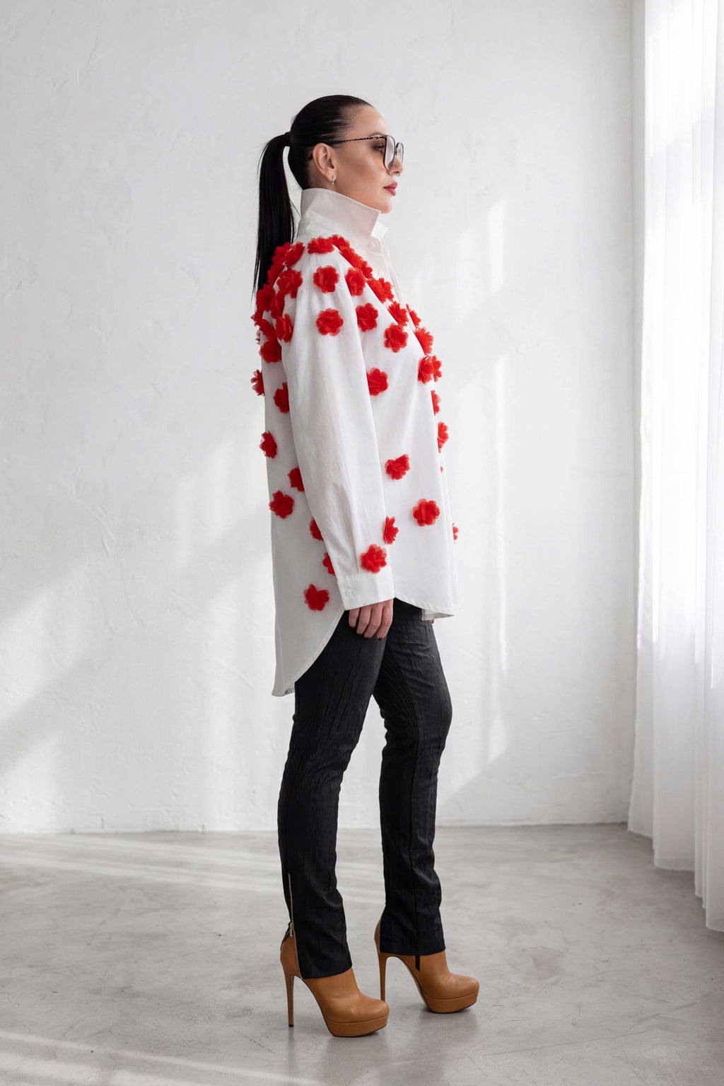 Woman wearing a white coat with red floral patterns in a minimalistic setting