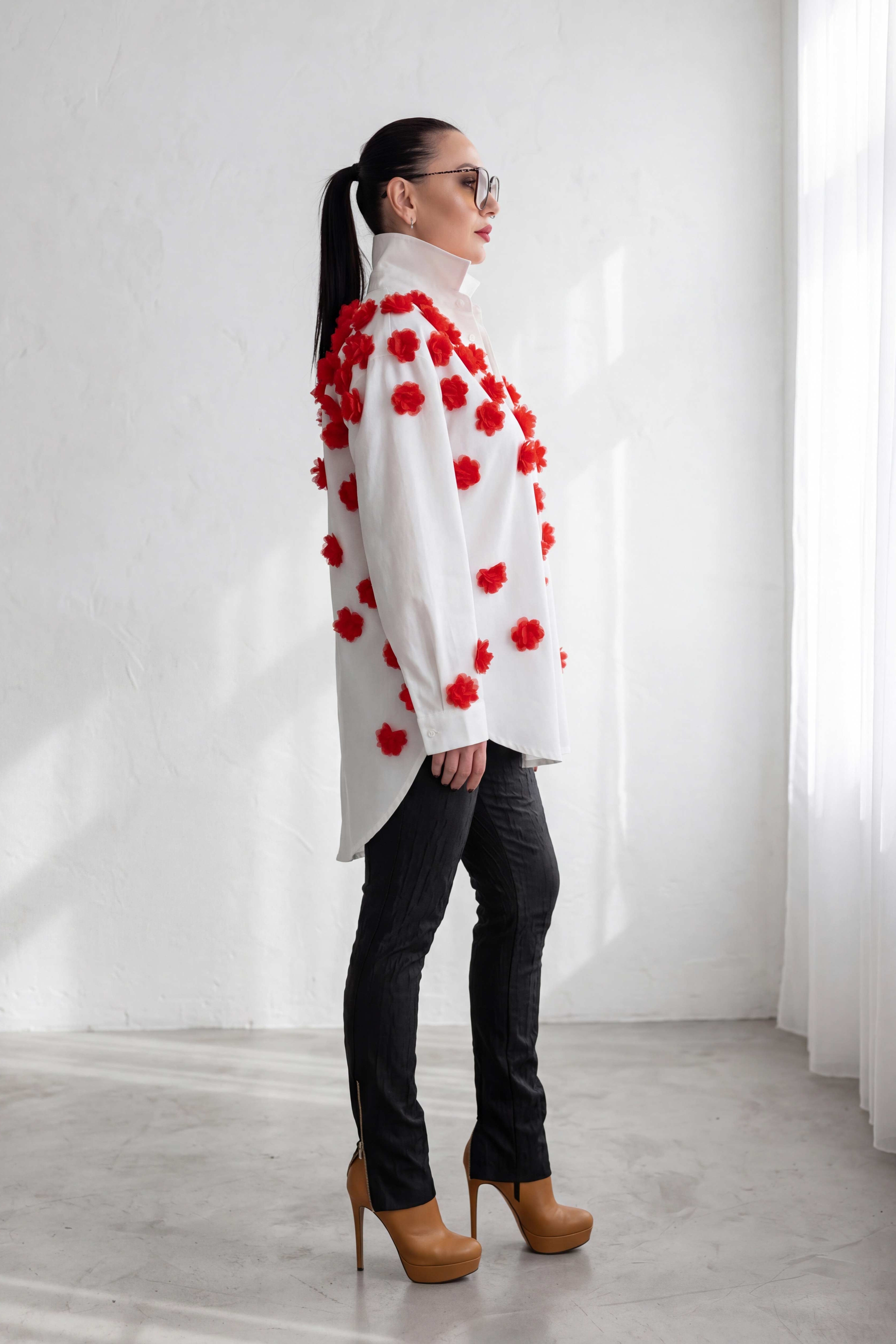 Woman wearing a white coat with red floral patterns in a minimalistic setting