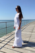 Woman in a white outfit standing on a wooden pier by the ocean