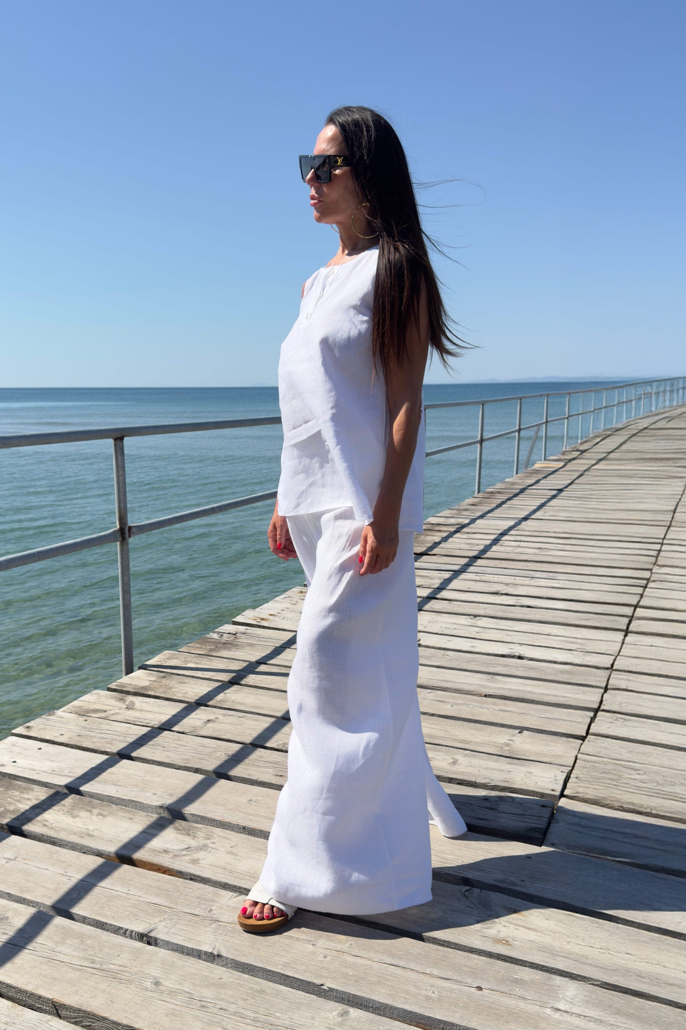 Woman in a white outfit standing on a wooden pier by the ocean