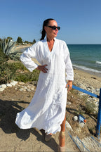 Woman in a white dress standing on a beach with ocean in the background