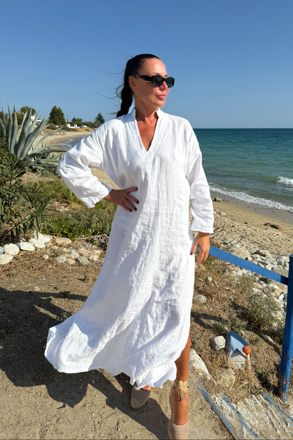 Woman in a white dress standing on a beach with ocean in the background