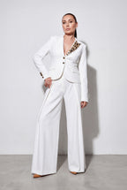 Woman wearing a white suit with decorative elements on a plain background