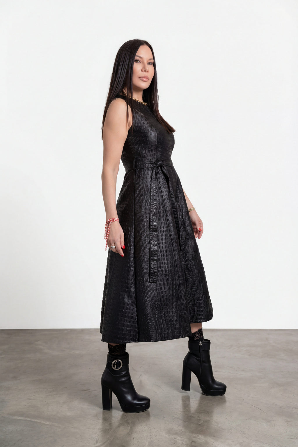 Woman wearing a black dress with a belt standing on a gray floor against a white wall