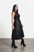 Woman wearing a black dress with a belt standing on a gray floor against a white wall